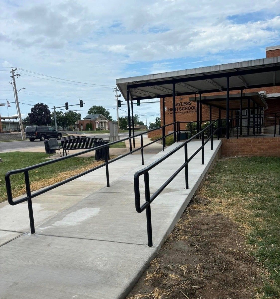 Accessible ramp with black handrails leading to a brick building entrance under a covered awning.
