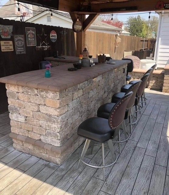 Outdoor bar with stone counter, stools, and wooden deck under a shaded patio cover