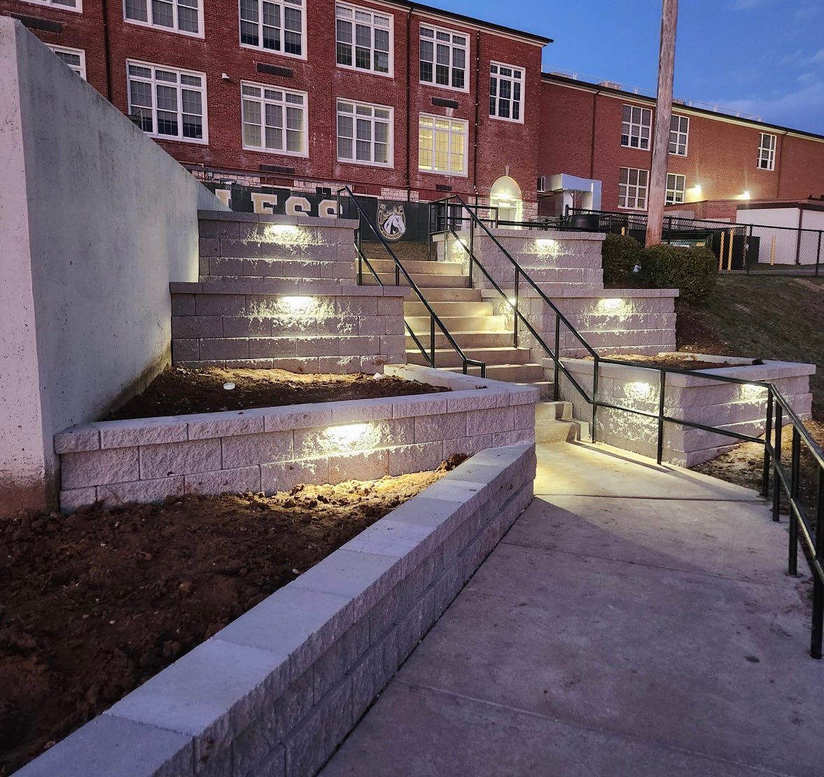 Outdoor brick steps and ramps leading to a lit building at dusk