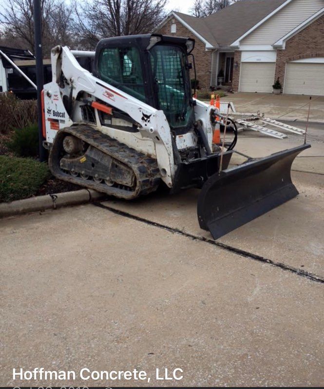 Compact track loader grading concrete driveway beside a house, with Hoffman Concrete, LLC watermark