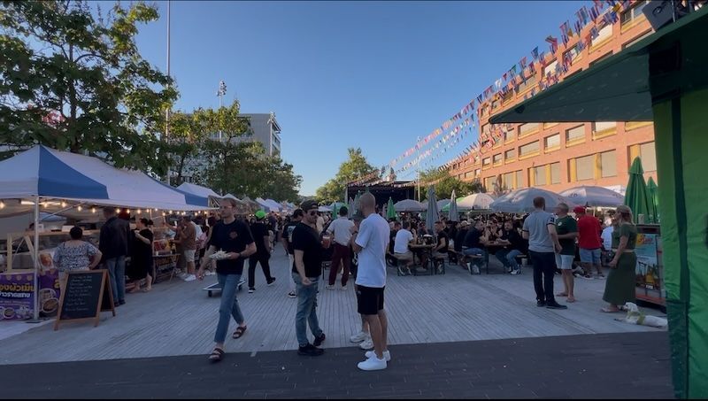 Crowds walk through a lively outdoor food market with white vendor tents. The busy evening scene shows another reason Switzerland is worth visiting beyond its countryside and mountain views.