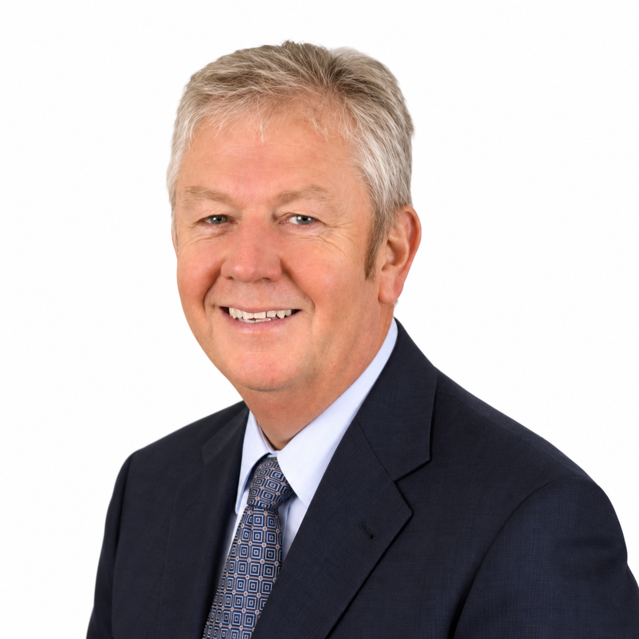 Professional headshot of a smiling man in a dark suit and patterned tie on a white background