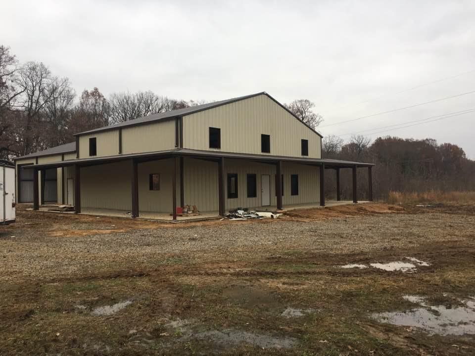 A beige, two-story metal building with a wrap-around porch under construction on a dirt lot.