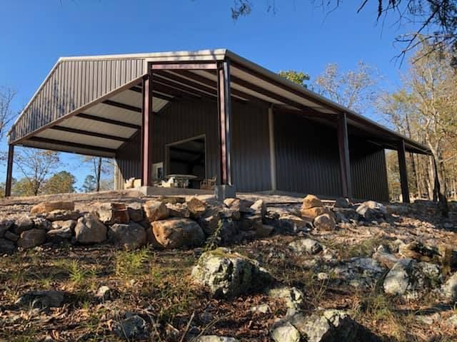 A large metal building with a porch is sitting on top of a rocky hill.