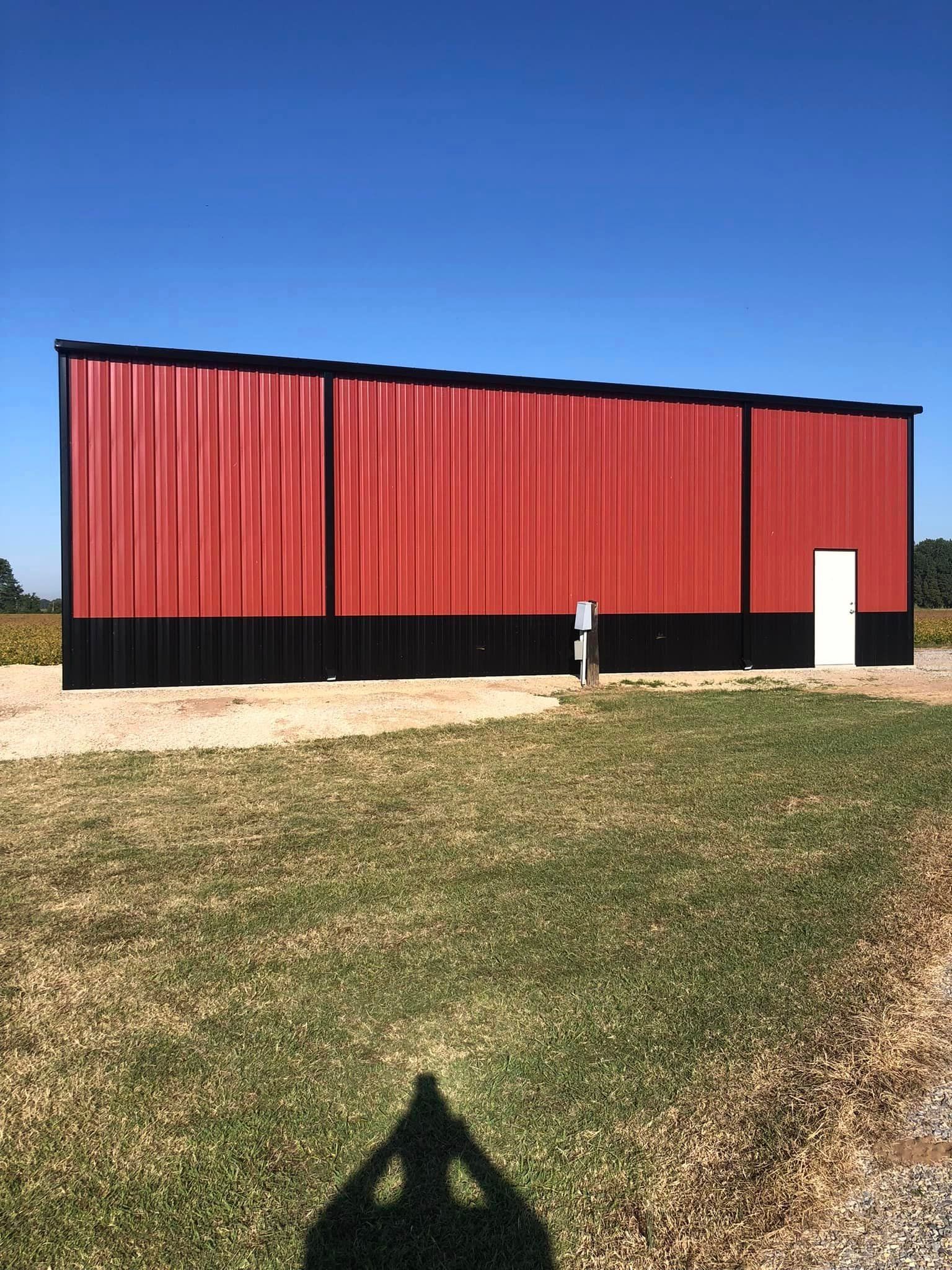 A large red barn is sitting in the middle of a grassy field.