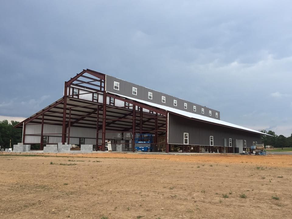 A steel-frame building under construction with a raised clerestory roof section against a cloudy sky.