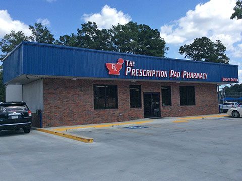 The Prescription Pad Pharmacy with a blue roof and brick exterior under a blue sky with white clouds.