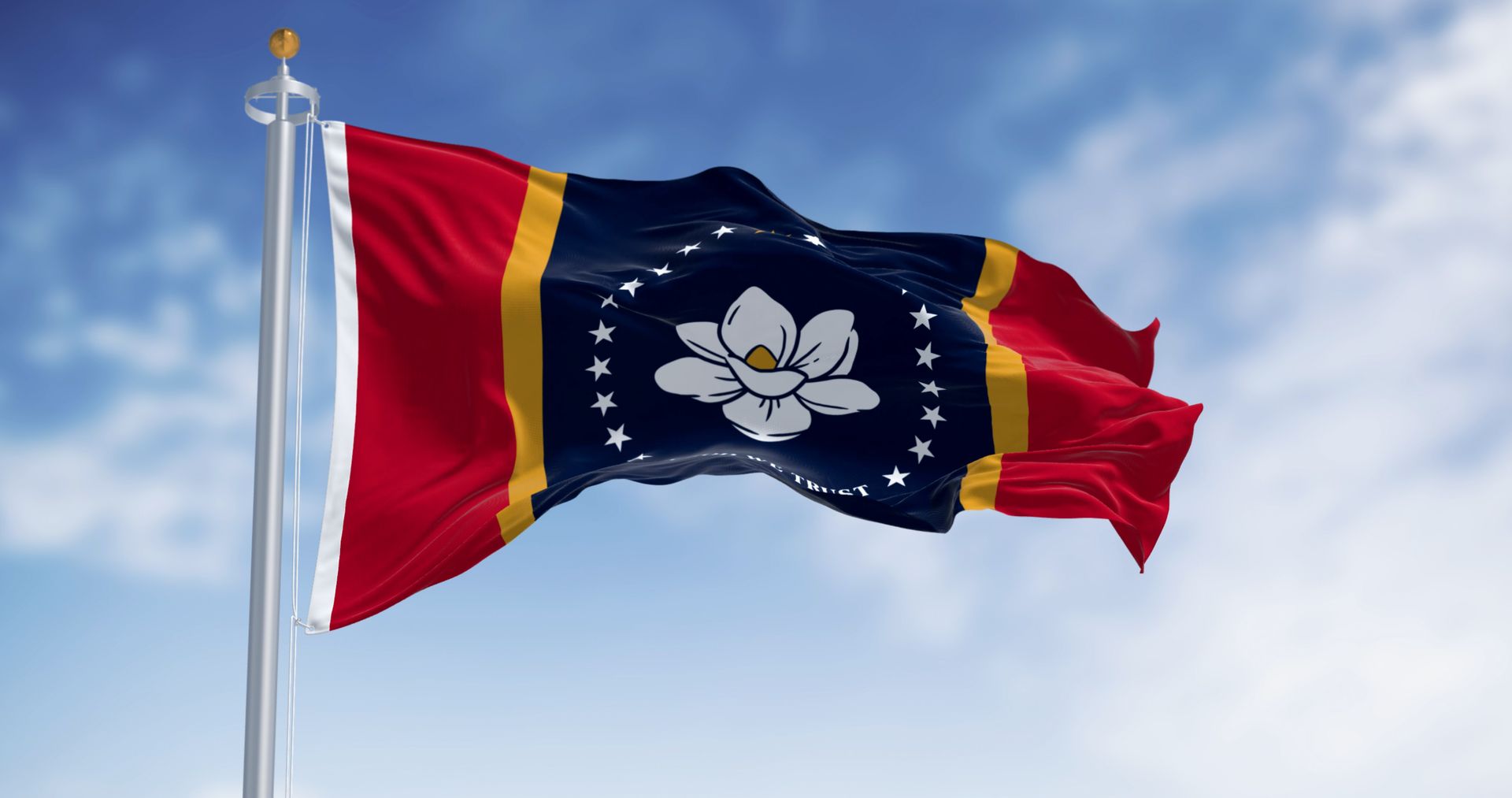 The Mississippi state flag, featuring a white magnolia blossom and stars on a blue field flanked by red and gold, waving.