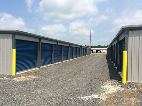 A row of storage units with blue doors on a gravel road.