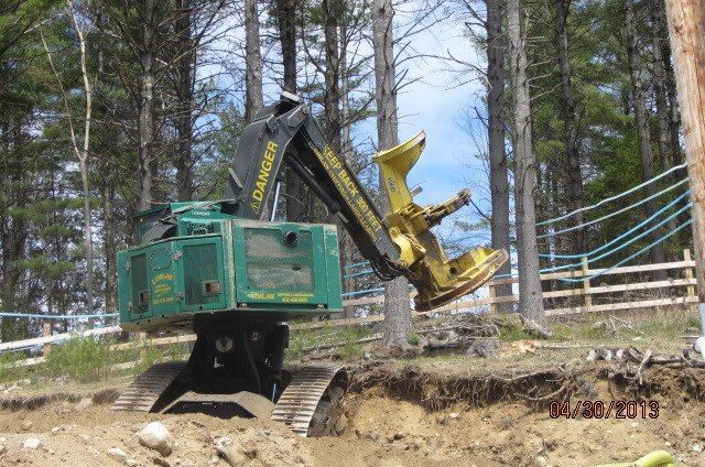 A green and yellow loader is sitting in the dirt in the middle of a forest.