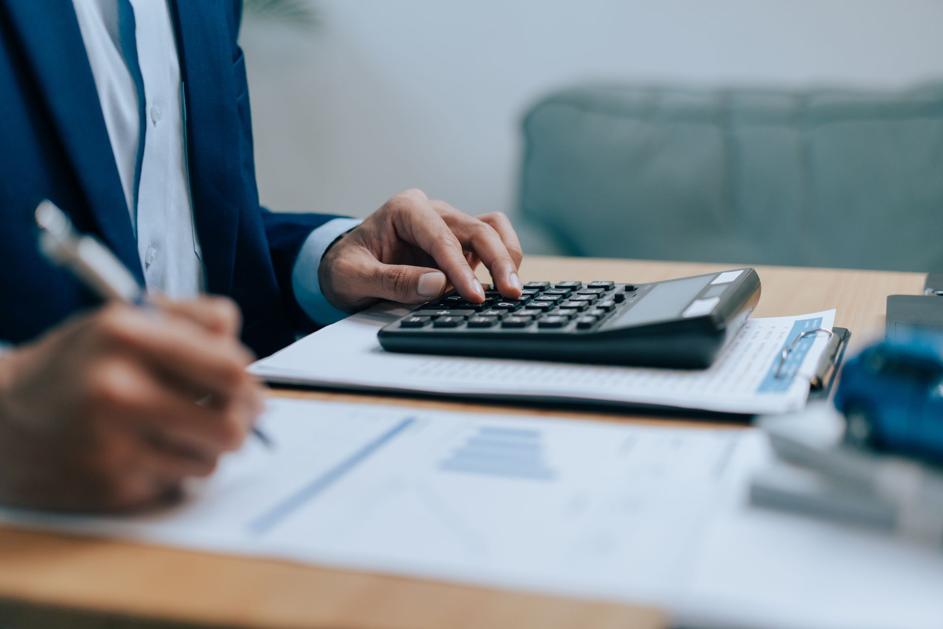 Close-up of a local tax accountant using a calculator and writing on a document for a report.