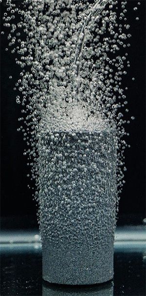 Air bubbles rising from a cylindrical stone in water against a dark background.