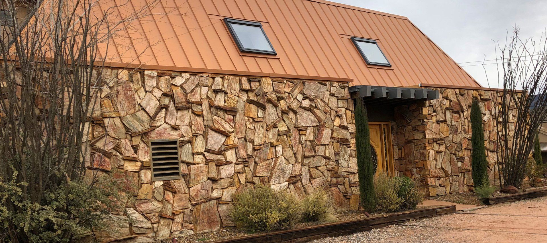 Stone building with a copper roof, small skylights, and a wooden door.