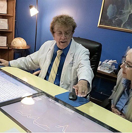 Man in lab coat points to a computer screen; woman looks on. Room is blue, with various equipment.