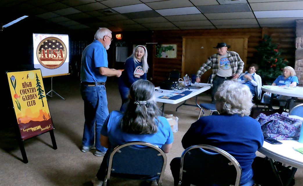 People at an event, some seated, others standing at tables, with display paintings and a decorative tree in a room.