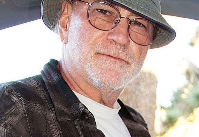Man wearing glasses, a hat, and a plaid shirt, looking towards the camera.