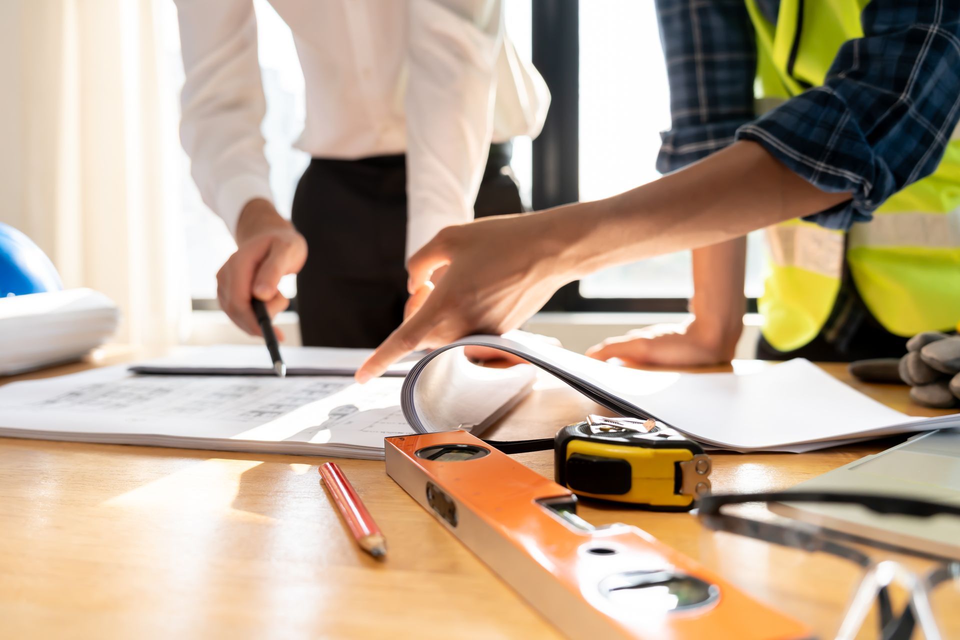 Construction workers reviewing plans at a table with tools and a measuring tape
