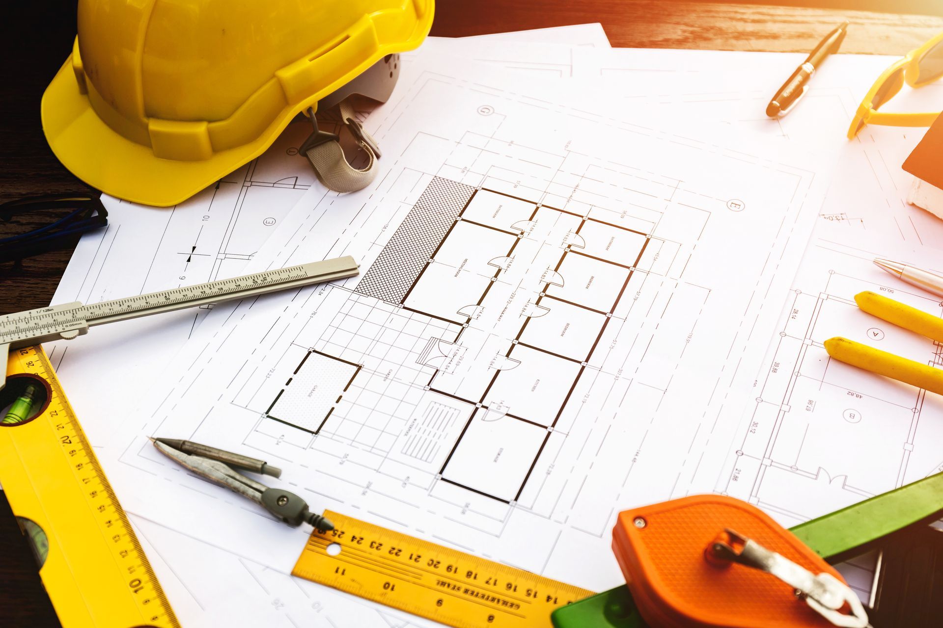Architectural floor plan with yellow hard hat, rulers, pencil, and drafting tools on a desk