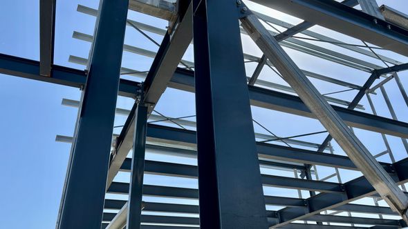 Construction worker in hard hat and harness inspecting wooden roof beams inside a building frame