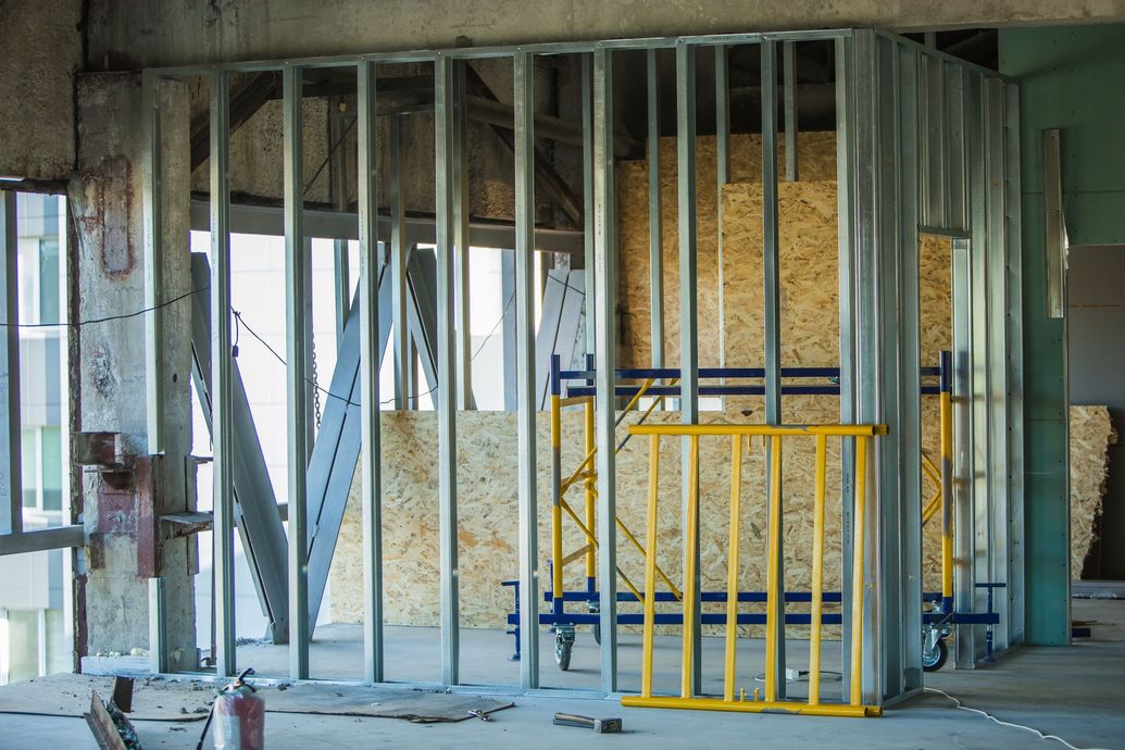 Construction site with wooden framing, excavator, and muddy ground beside a concrete foundation