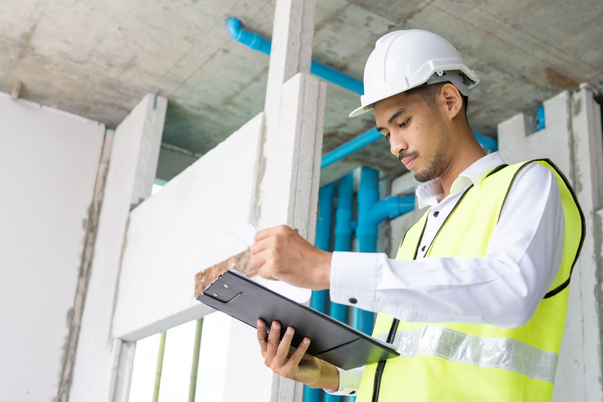 Construction worker in hard hat and safety vest taking notes on a clipboard at a building site