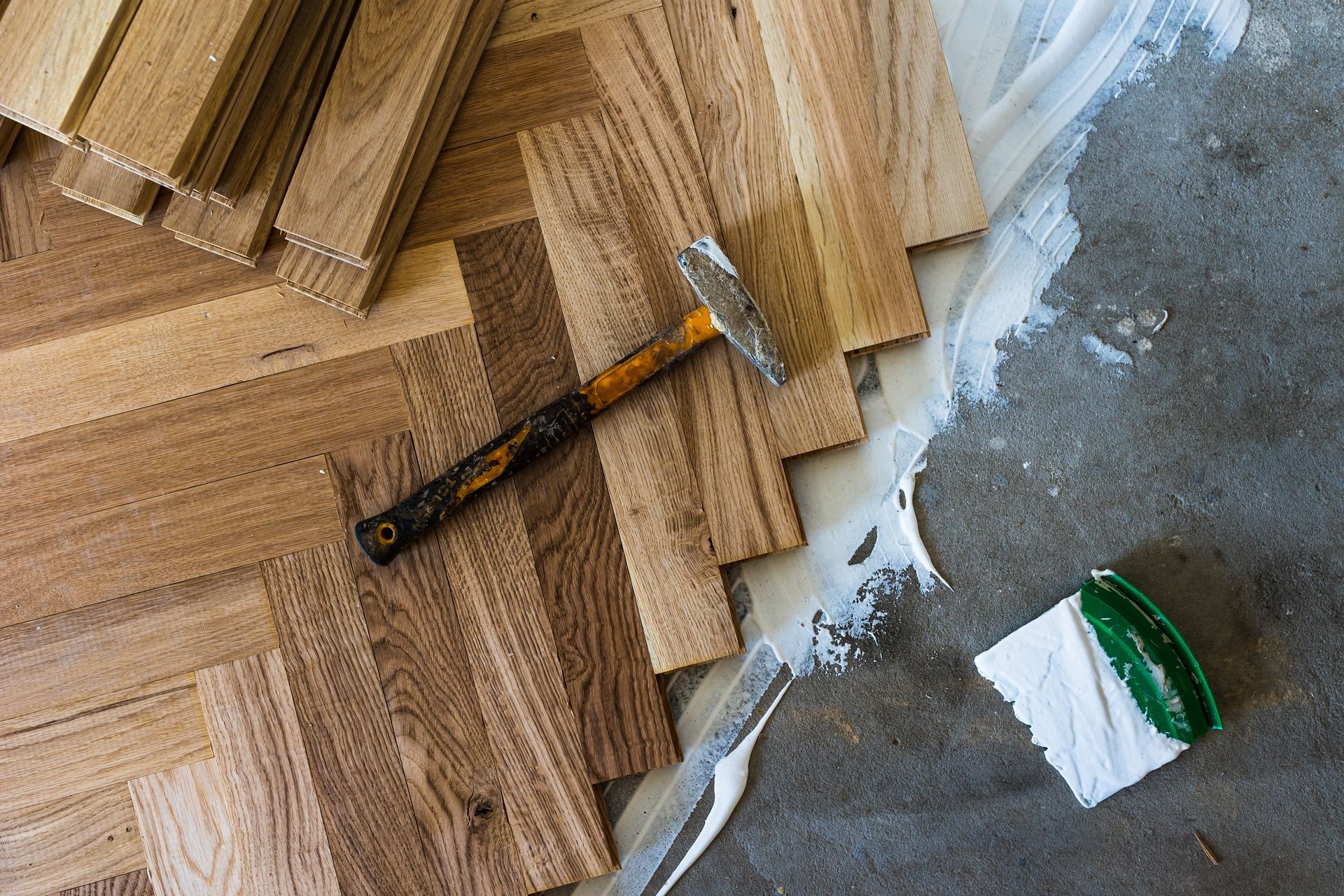 Hammer on stacked wood flooring planks beside a white bucket and concrete floor