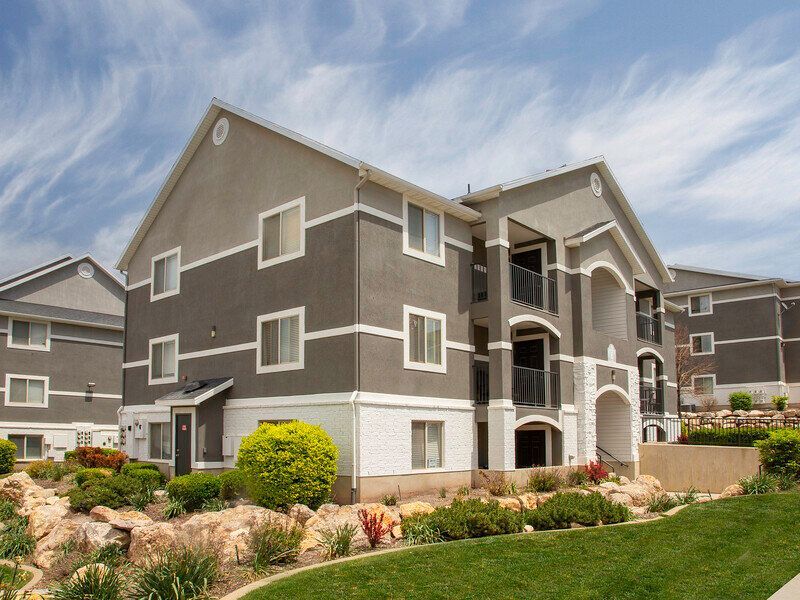 Modern apartment buildings with brown and beige siding, arched balconies, and landscaped grounds