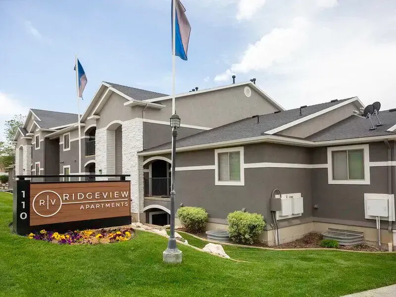Apartment building entrance with Ridgeview sign, gray exterior, flags, and landscaped lawn