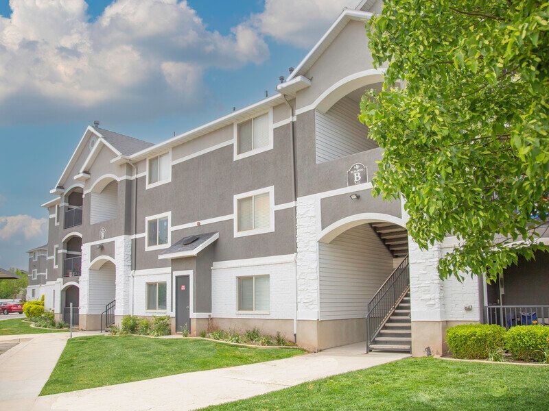 Apartment building exterior with gray and white siding, arched entrances, and a green lawn under a blue sky