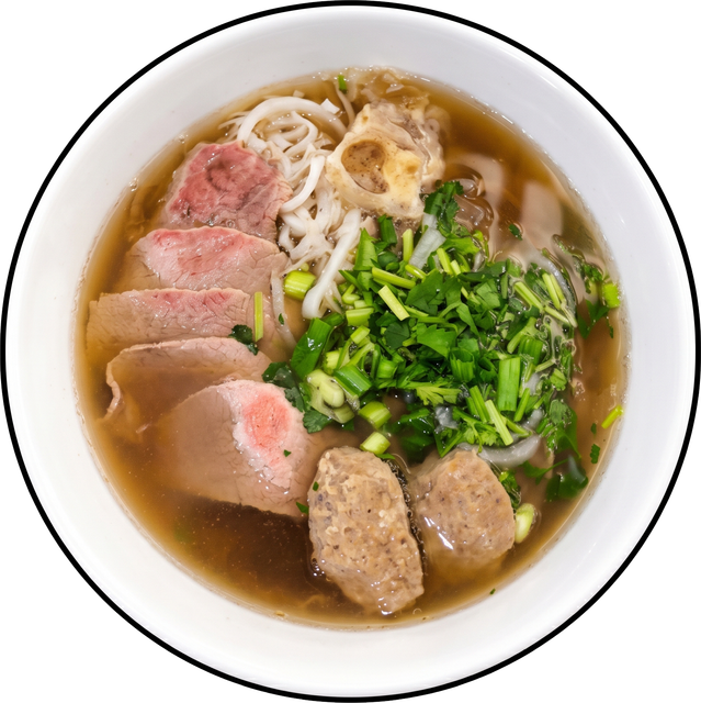 Bowl of beef noodle soup topped with sliced meat, meatballs, herbs, and scallions in broth