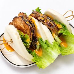 Grilled chicken and lettuce in soft steamed buns with orange sauce on a white plate