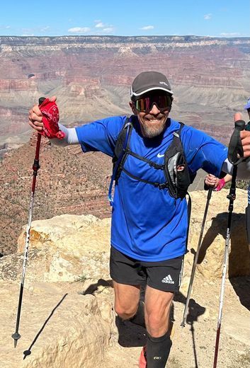 Hiker in blue shirt and black shorts standing with trekking poles at the Grand Canyon overlook