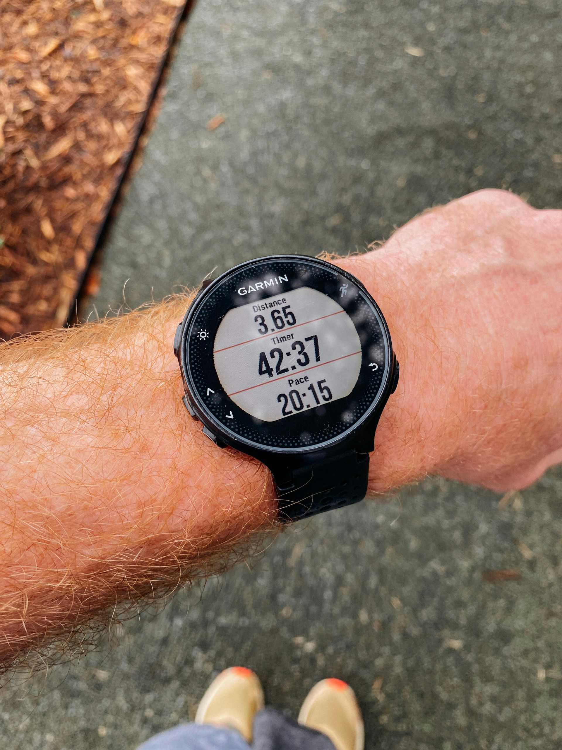 Close-up of a wrist wearing a black sports watch showing the time on a sidewalk.