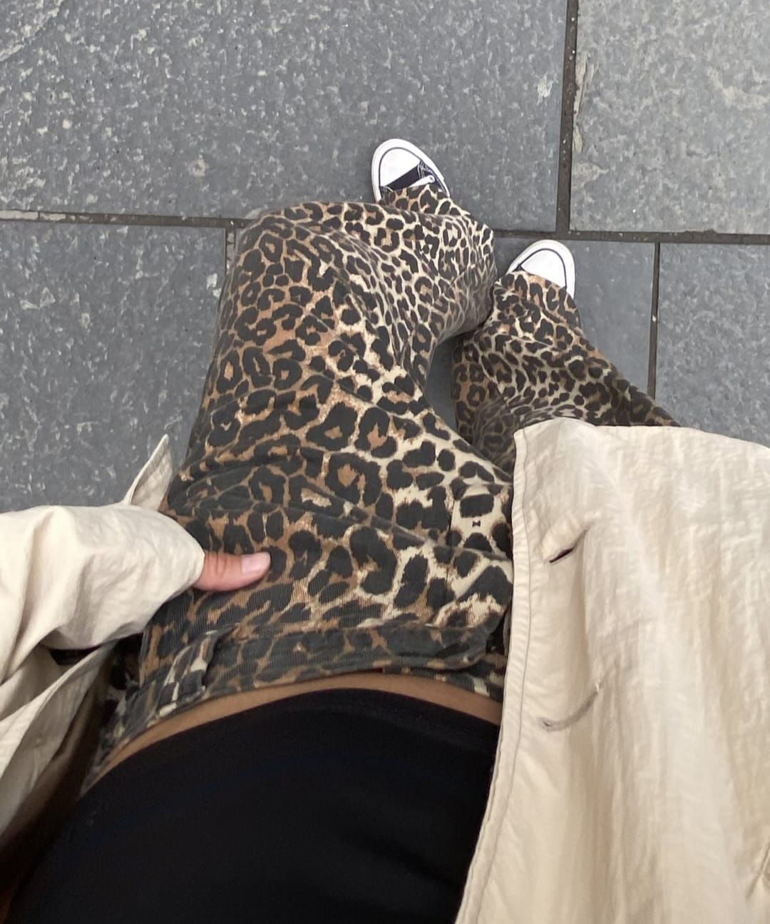 Falda con estampado de leopardo y top negro con zapatillas blancas sobre pavimento gris, vista desde arriba.