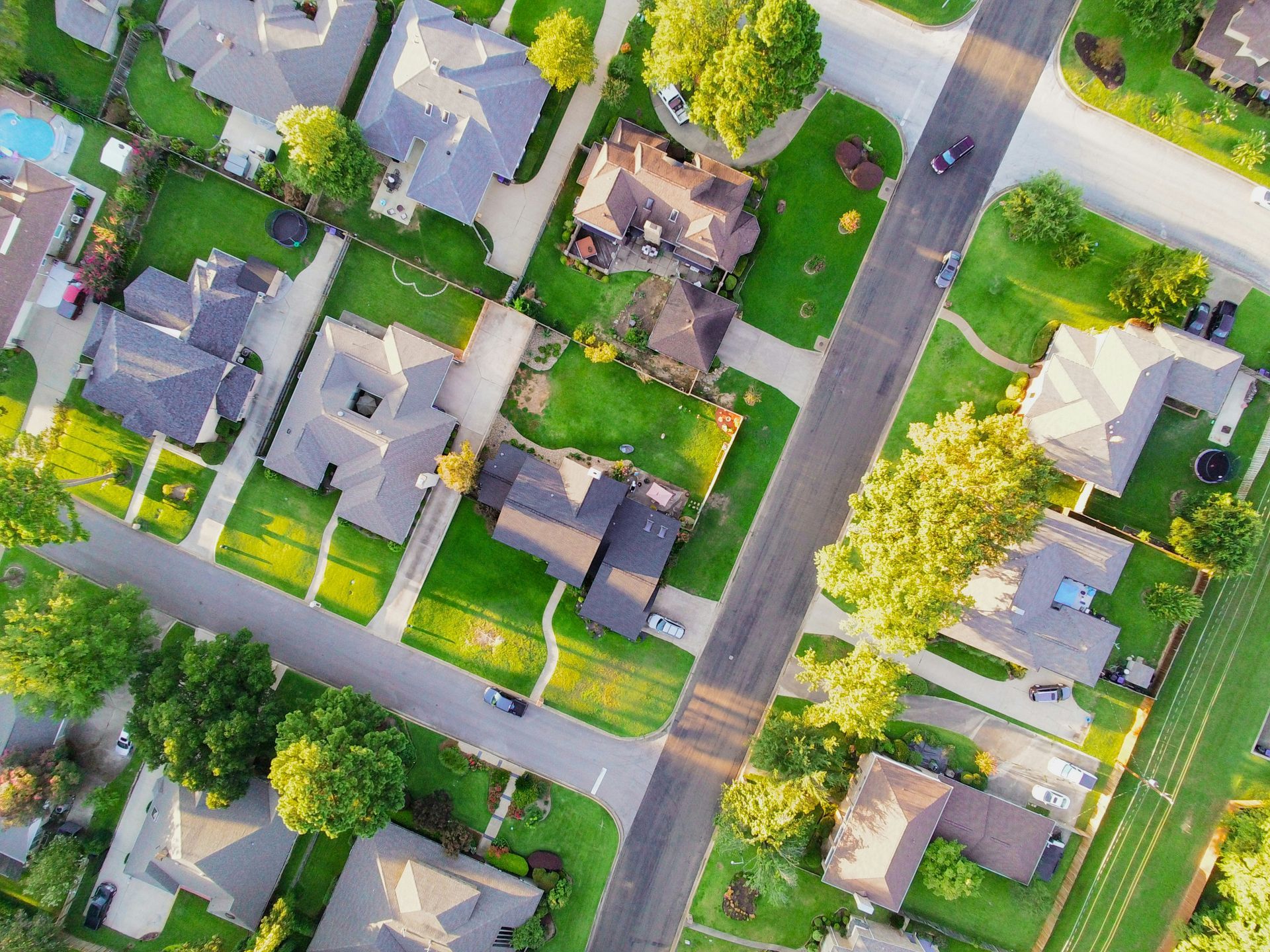 Aerial view of a suburban neighborhood with houses, driveways, trees, and intersecting streets.