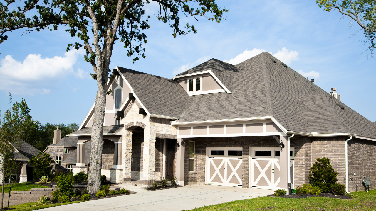 Large suburban brick house with a gray roof, double garage, and landscaped front yard.