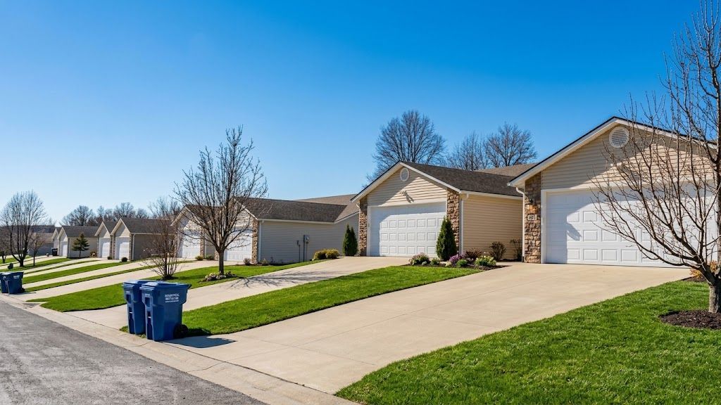 Suburban houses with driveways, green lawns, and blue recycling bins on a sunny day