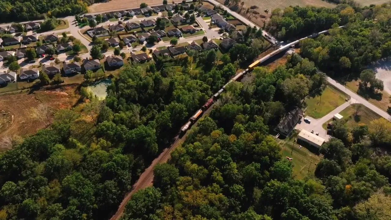 Aerial view of a wooded neighborhood with houses, a curving road, and a small white building.