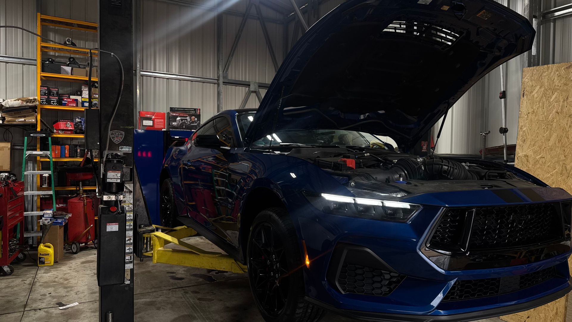 Blue Mustang on a lift in a garage, hood open. | Alberto's Transmissions & Auto