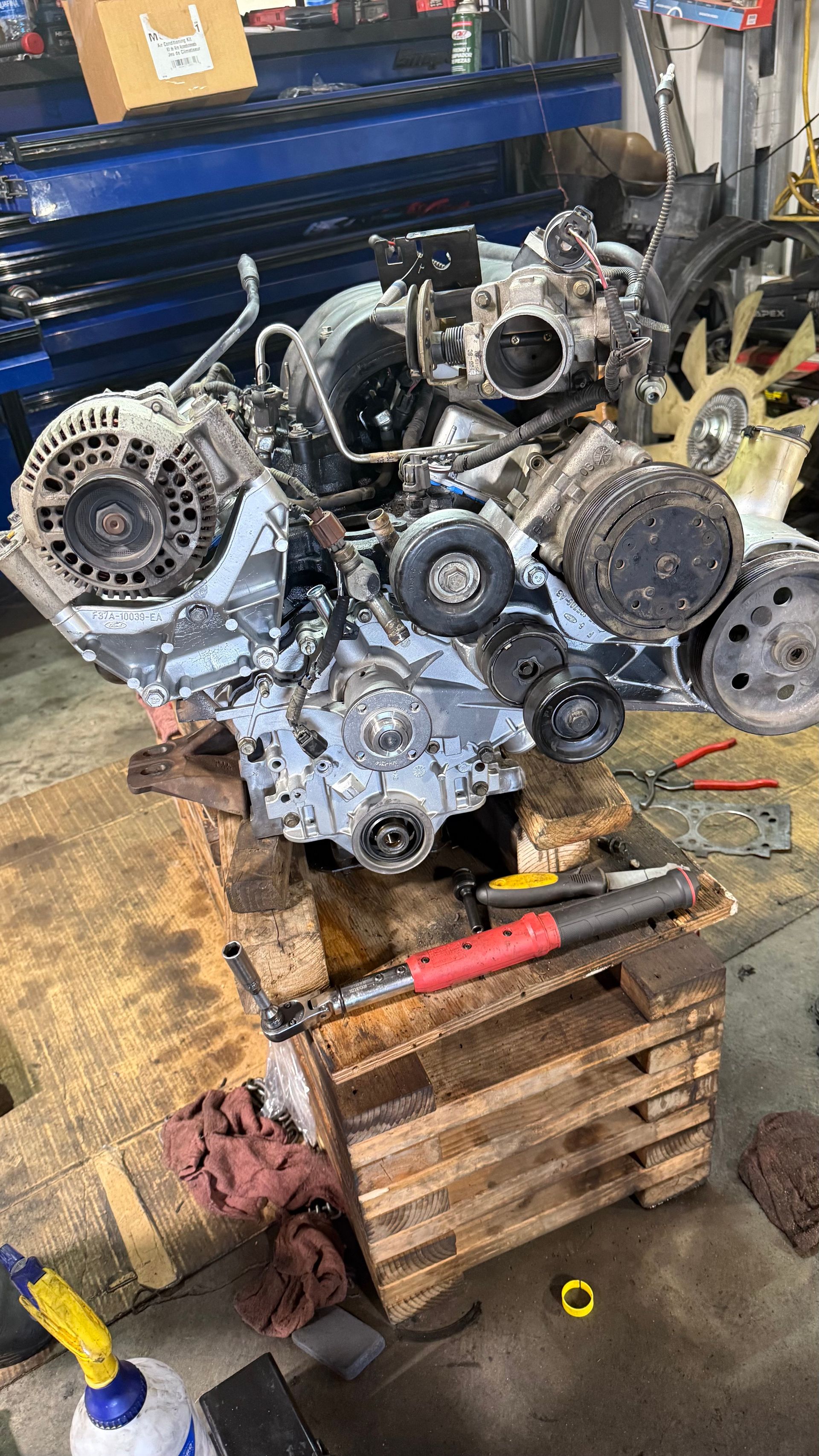 Car engine being worked on in a shop. It sits on a wooden pallet with tools nearby. | Alberto's Transmissions & Auto