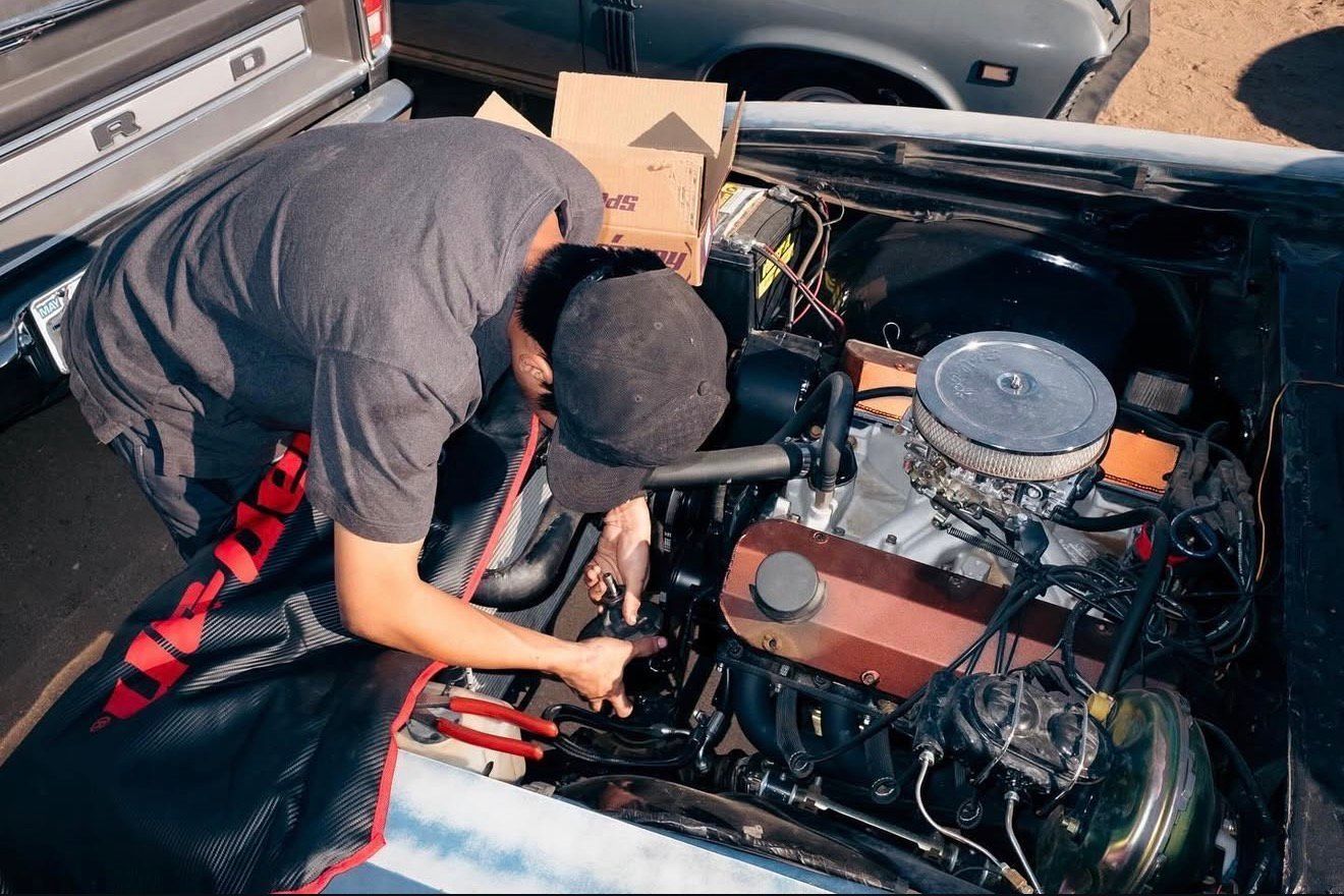 Man working on car engine in an outdoor setting. He's wearing a hat and pointing at a part. | Alberto's Transmissions & Auto