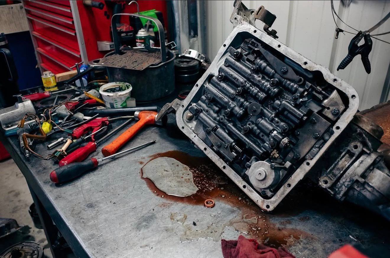 Transmission components on a workbench, oil spill. Tools and a container are nearby. | Alberto's Transmissions & Auto