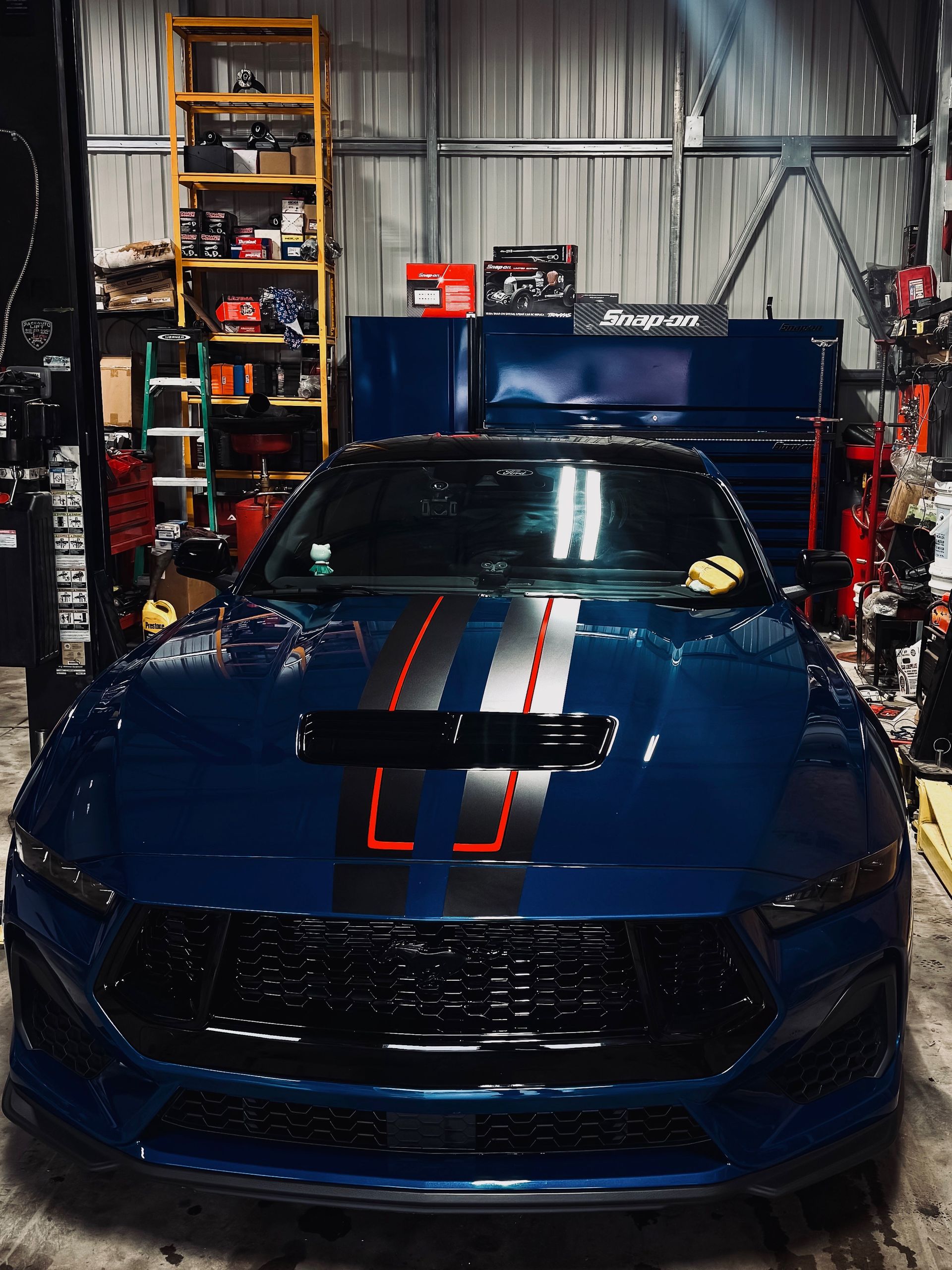 Dark blue Ford Mustang with racing stripes inside a cluttered garage. | Alberto's Transmissions & Auto