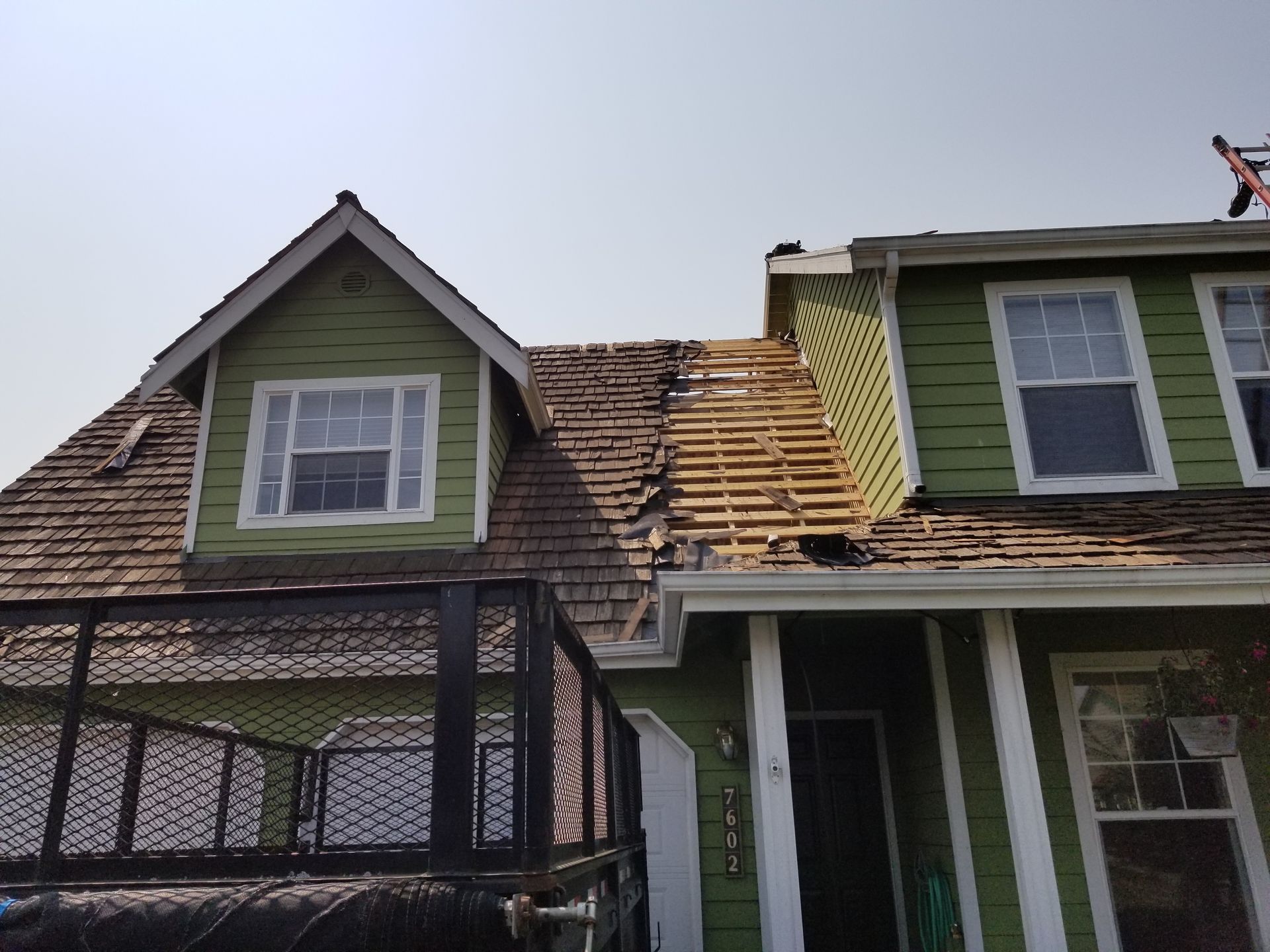 Damaged green house roof with missing shingles and exposed wood under bright daylight