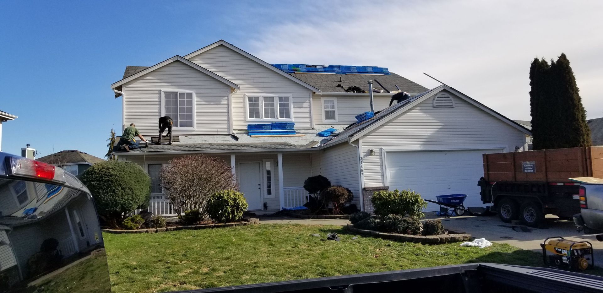 Suburban two-story house with white siding, garage, front lawn, and parked vehicles under a blue sky