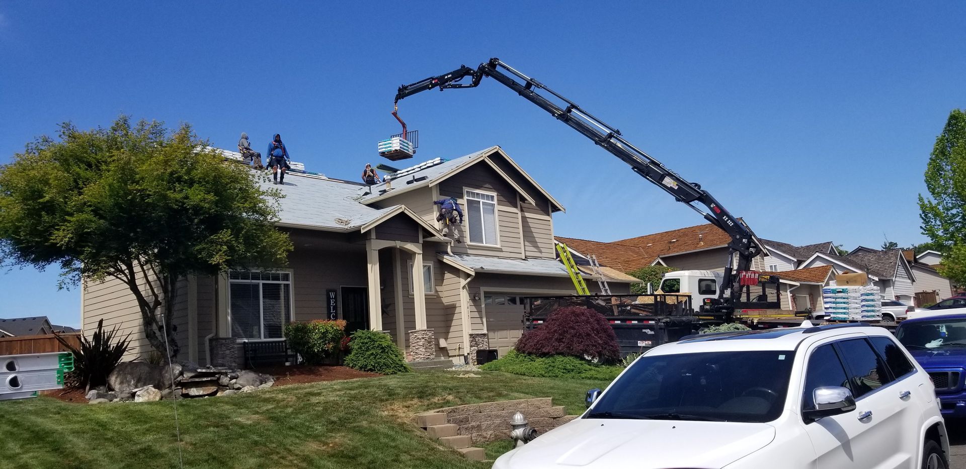 Crane removing roof debris from a damaged house with a white truck parked in front