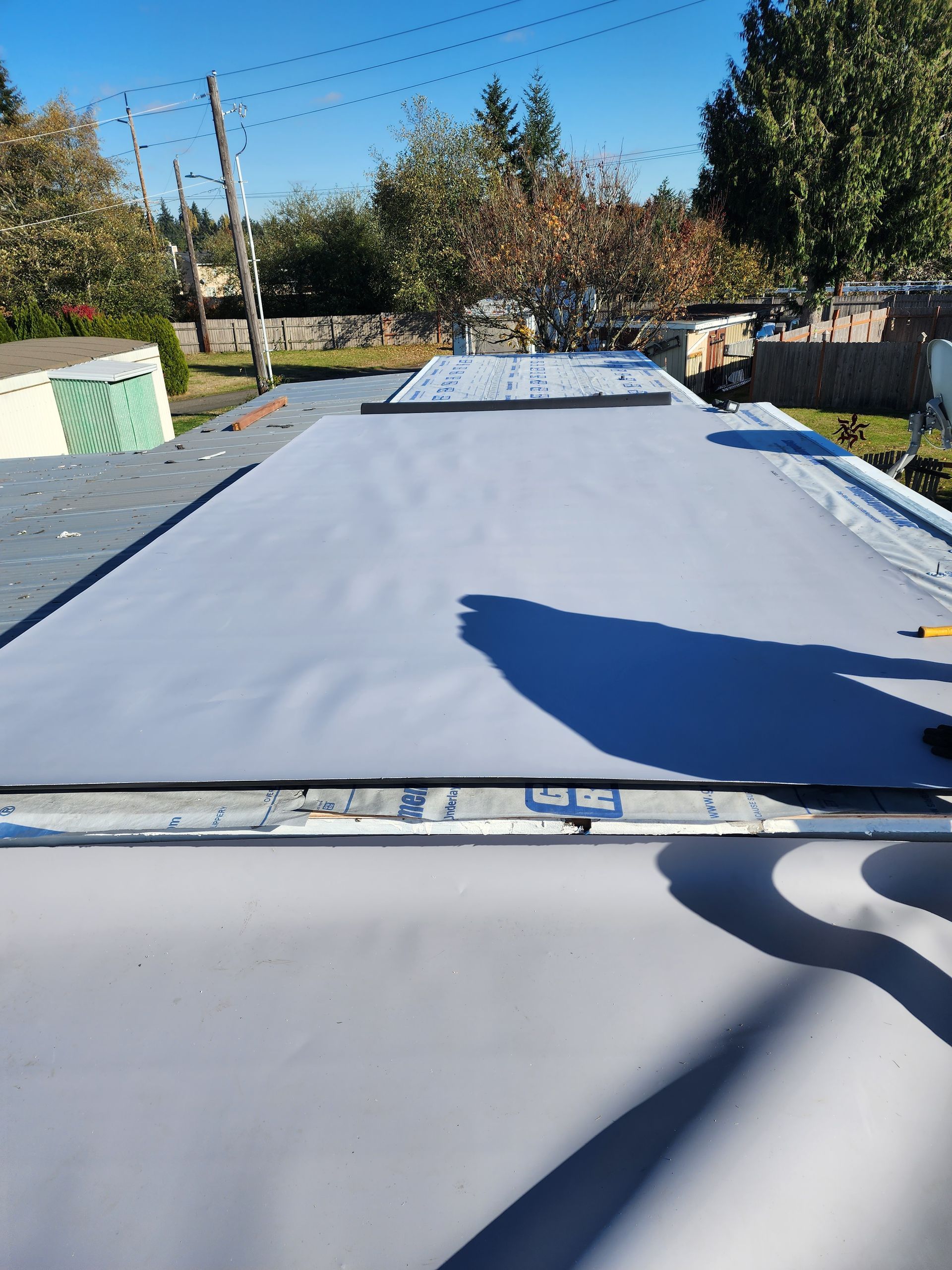Flat white roof membrane being installed on a building, with trees and a ladder in the background.