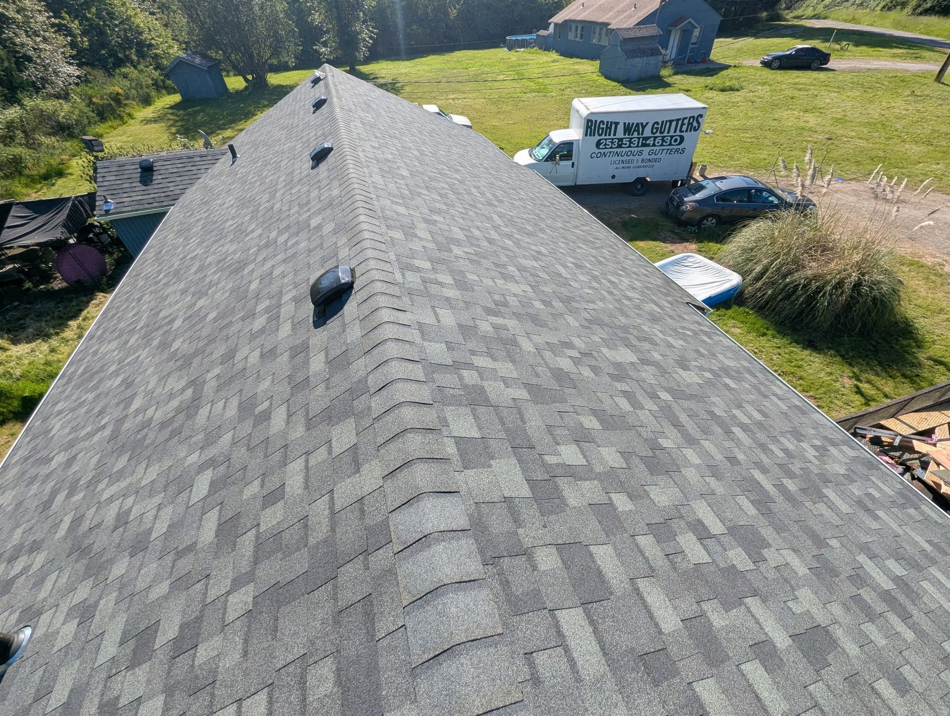 Roof view with gray shingles and roof vents, overlooking a grassy yard and neighboring houses.