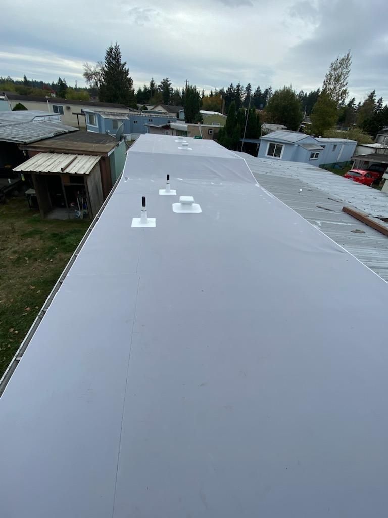 Long white rooftop with vents in a trailer park under a cloudy sky