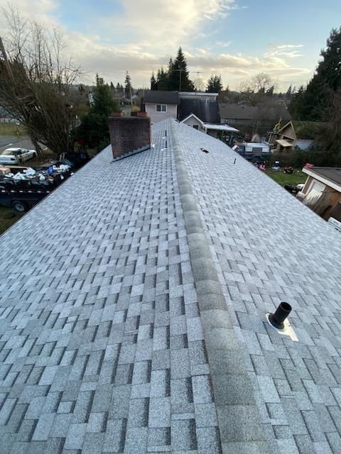 View from a roof ridge with gray shingles, chimney, and suburban homes at dusk